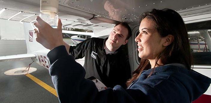 A flight instructor works with an aviation student outside the airplane
