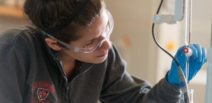 A student wearing rubber gloves and safety glasses while using equipment in chemistry lab