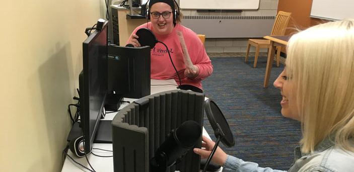 Two students laugh as they work together to record audio in the podcast studio.