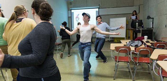 an acting class with the students walking in a circle with their arms out wide; one looks like he's walking on a catwalk or runway while others walk with looser posture